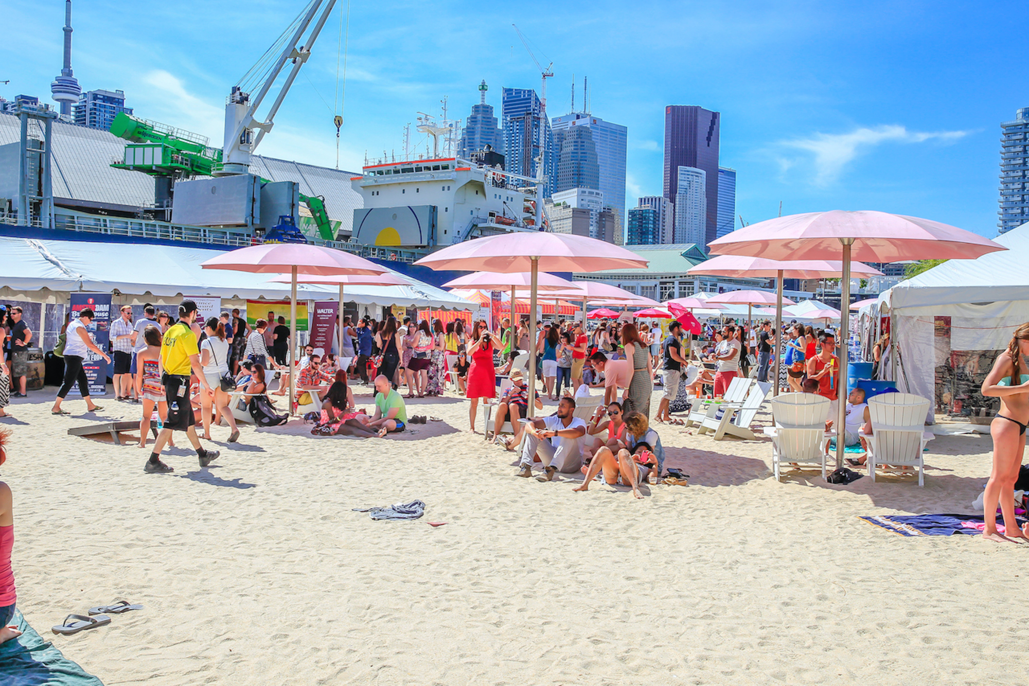 groups of people enjoying a summer day at a festival on a sandy beach with pink umbrellas