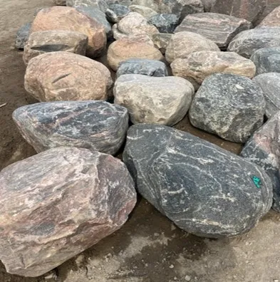 A collection of large glacial erratic stones in varying shades of grey, pink, and black, with visible veining and texture.