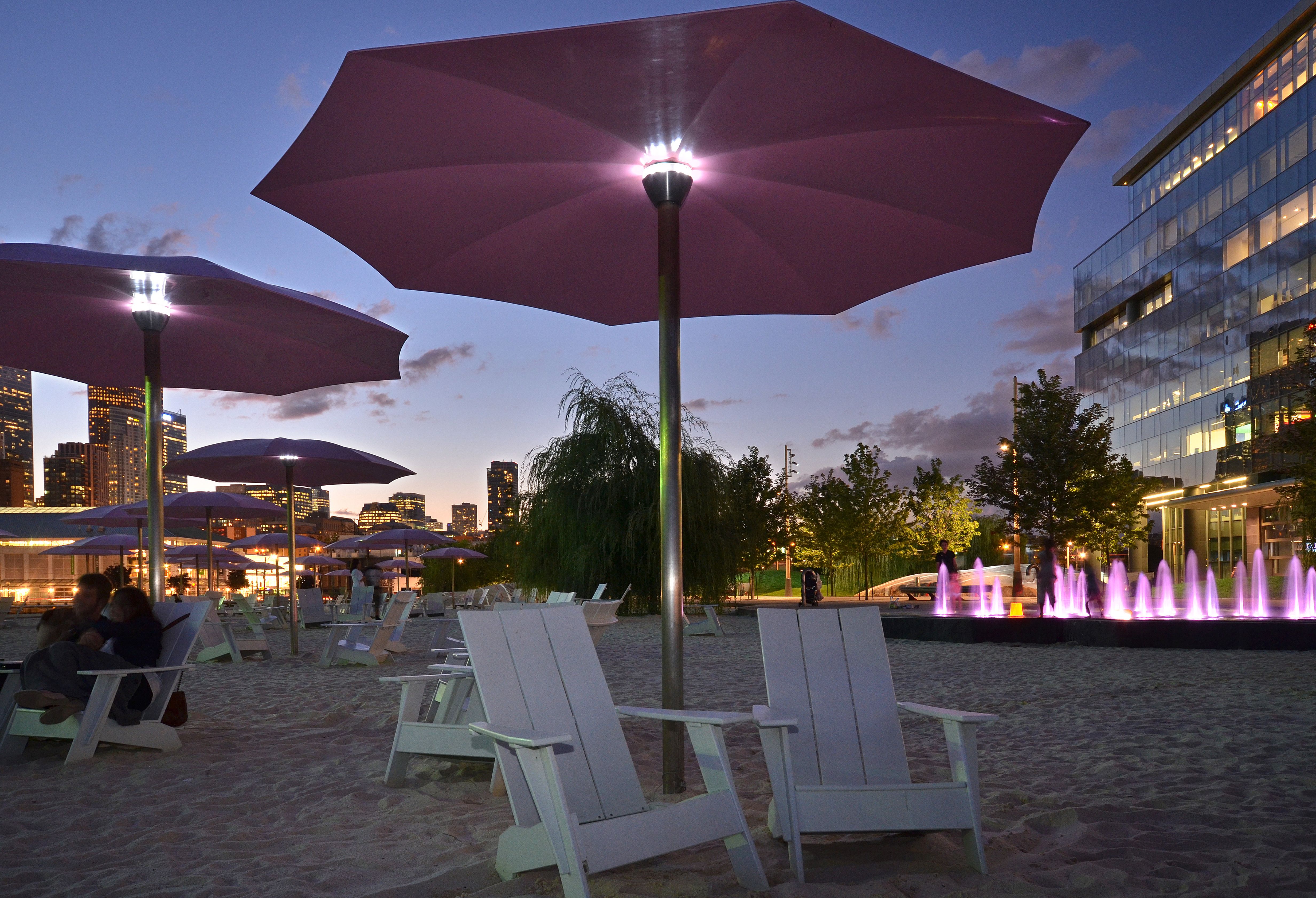 showing pink umbrellas, white Muskoka chairs and sandy beach lit up at dusk