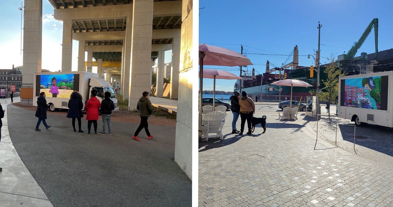 people strolling the waterfront on a sunny day and visiting a truck with a video display