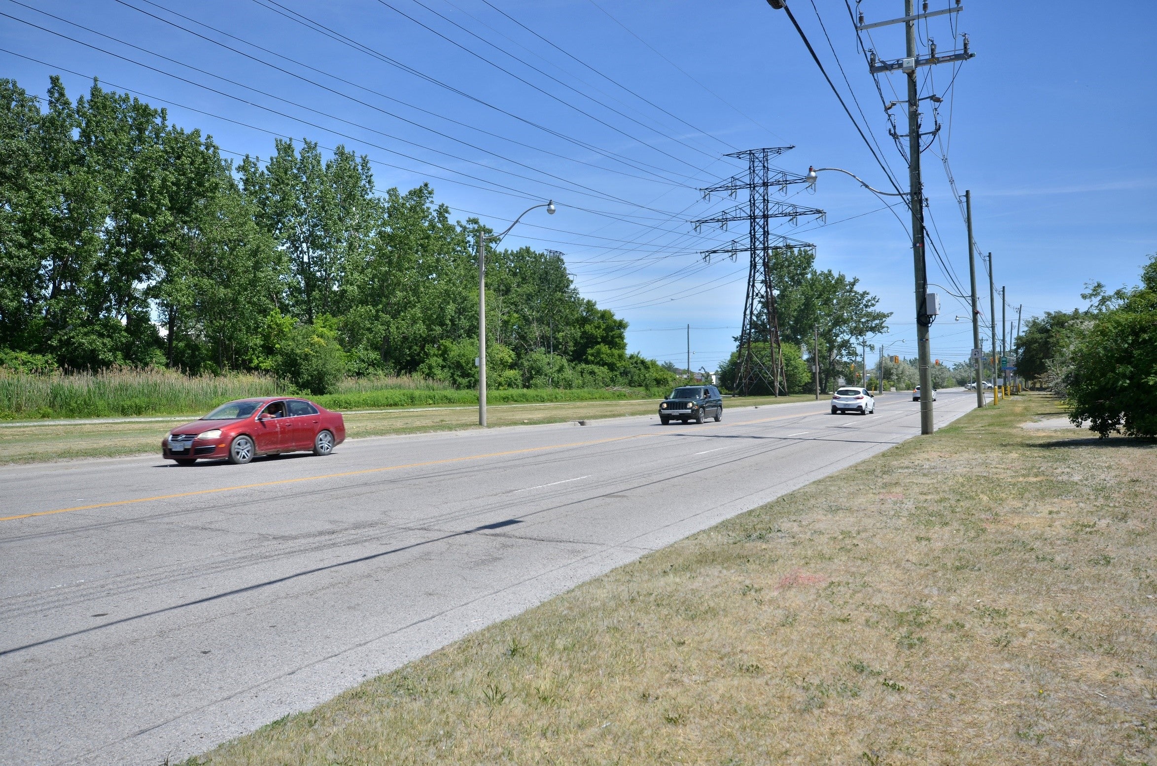 Cars driving along a wide open street with hydro lines