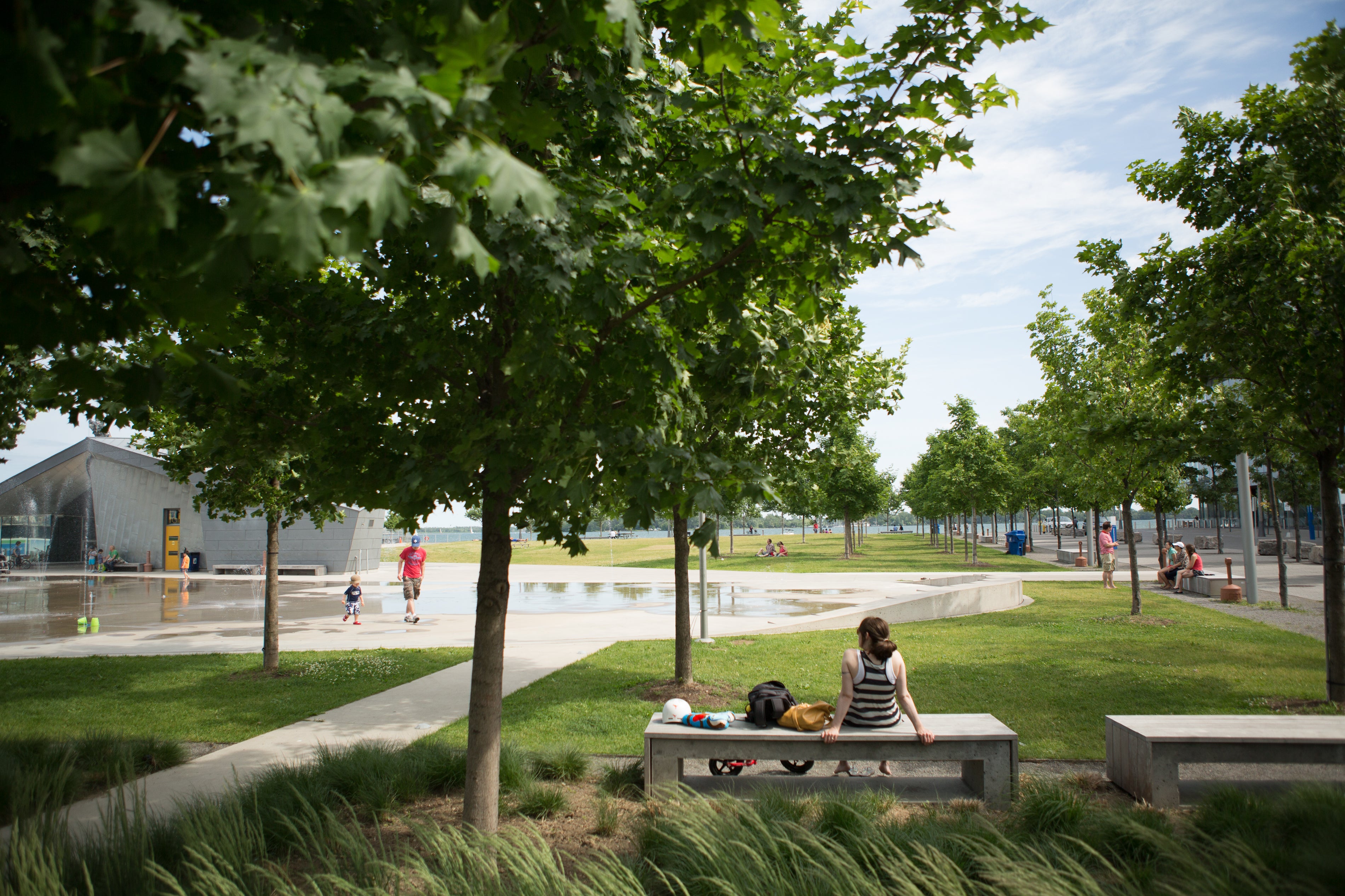 people sitting on a park bench next to a shaded area and splash pad