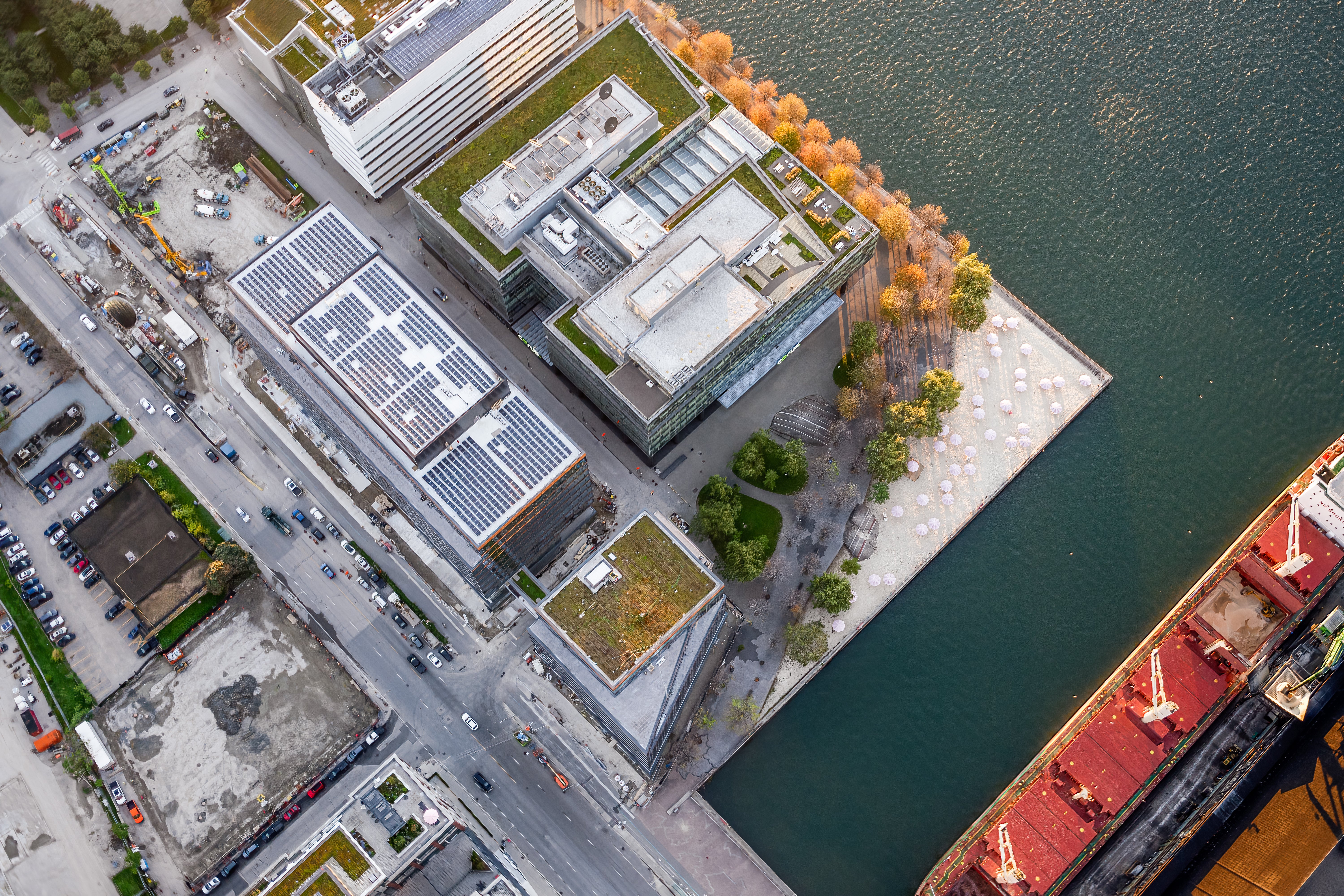 An aerial view of multiple buildings on the water's edge - one showing solar panels on the roof, and another with a green roof.