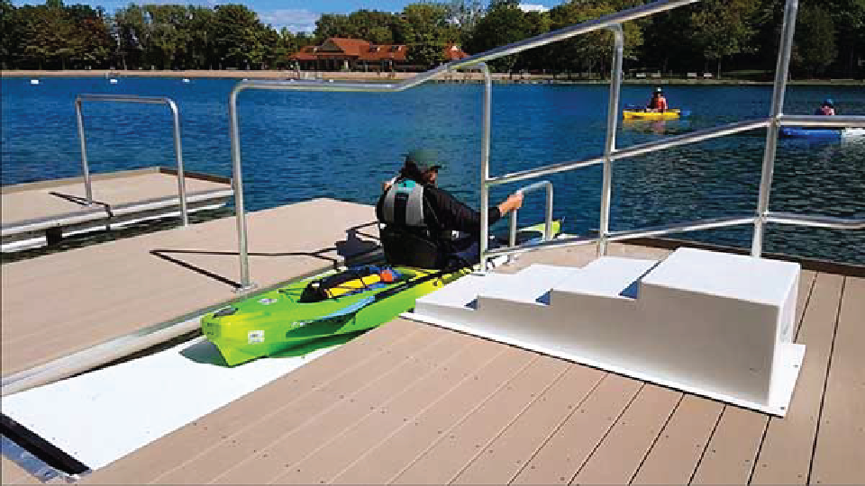 A kayaker enters the water from an accessible dock.