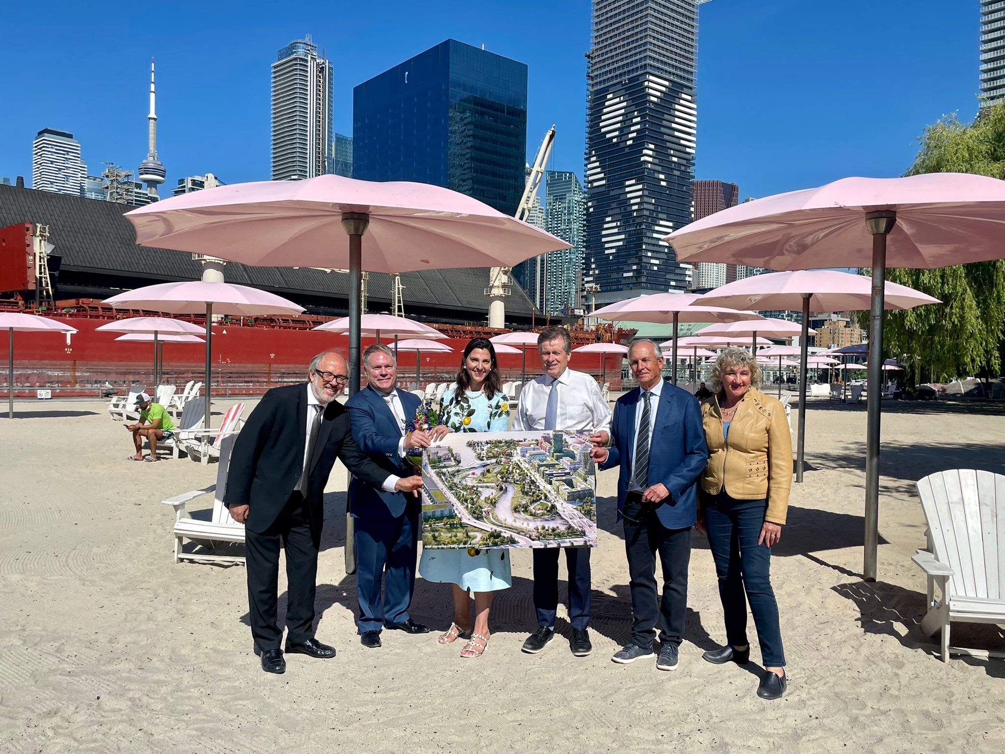 people standing on a beach under pink umbrellas, holding a large photo