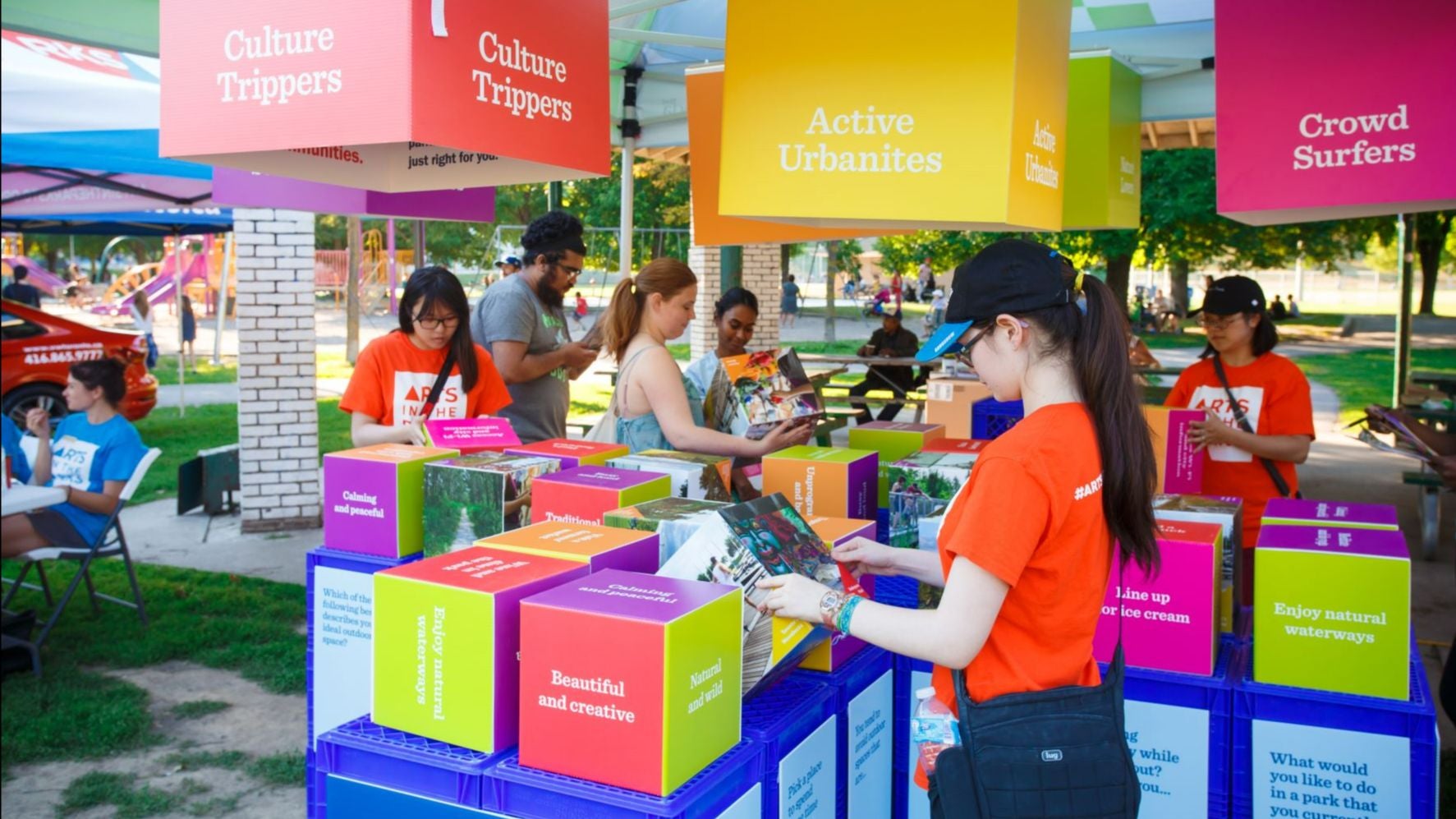 people gathered under a tent looking at colourful displays sitting on top of milk crates