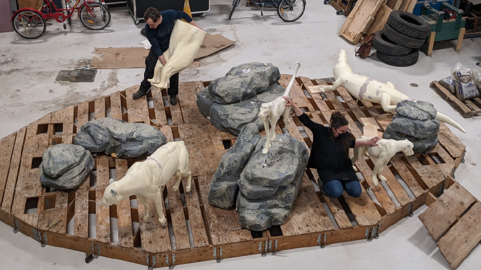 Two people placing model rocks and animals on a wooden platform.