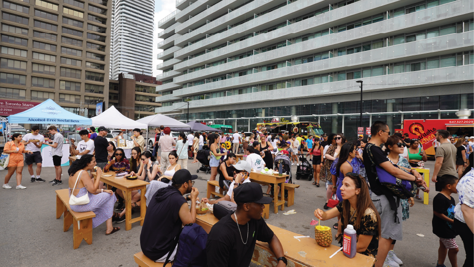 A busy outdoor food market, with apartment and office buildings in the background. 
