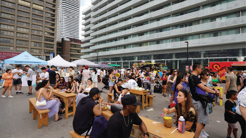 A busy outdoor food market, with apartment and office buildings in the background.