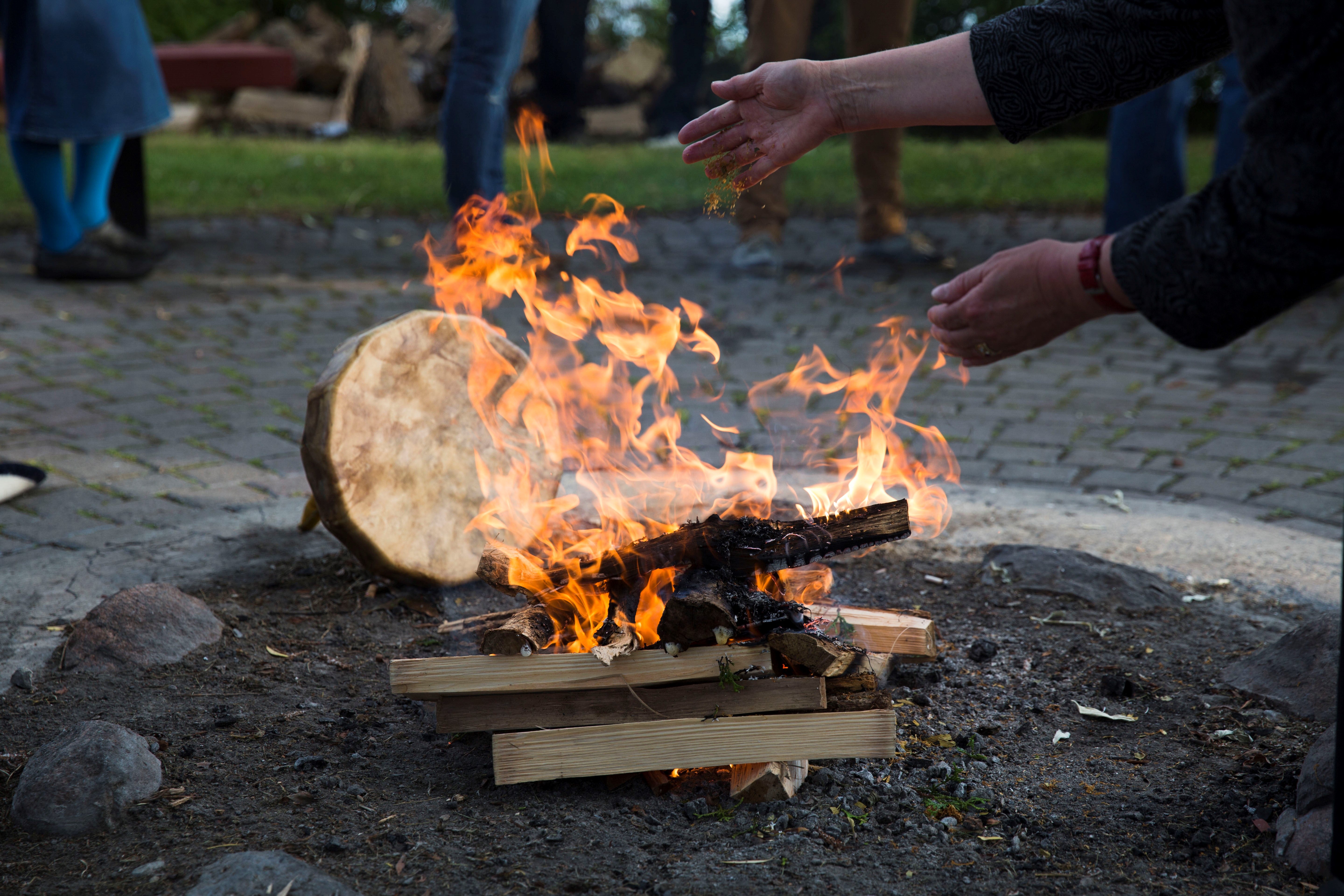 Two hands tending to a fire. A Hyde drum is behind the fire. 