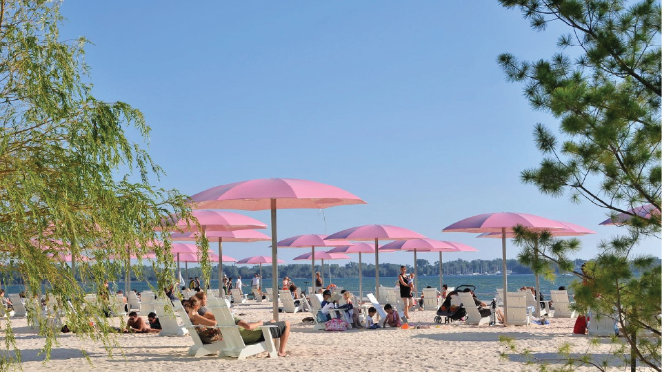 A crowded beach on a summer day. People sitting under pink umbrellas.