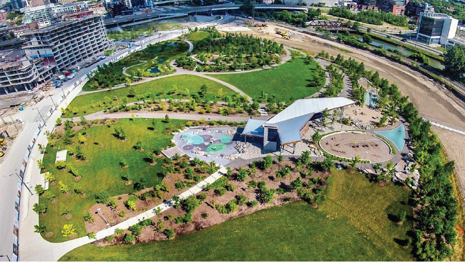 Aerial photo of a city park surrounded by apartment buildings and a river. 