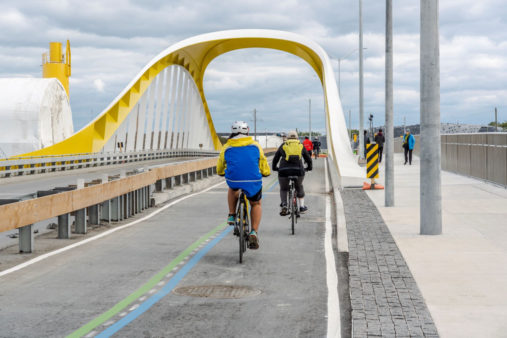 Cyclists ride in a separated bike lane through a yellow and white arched bridge.