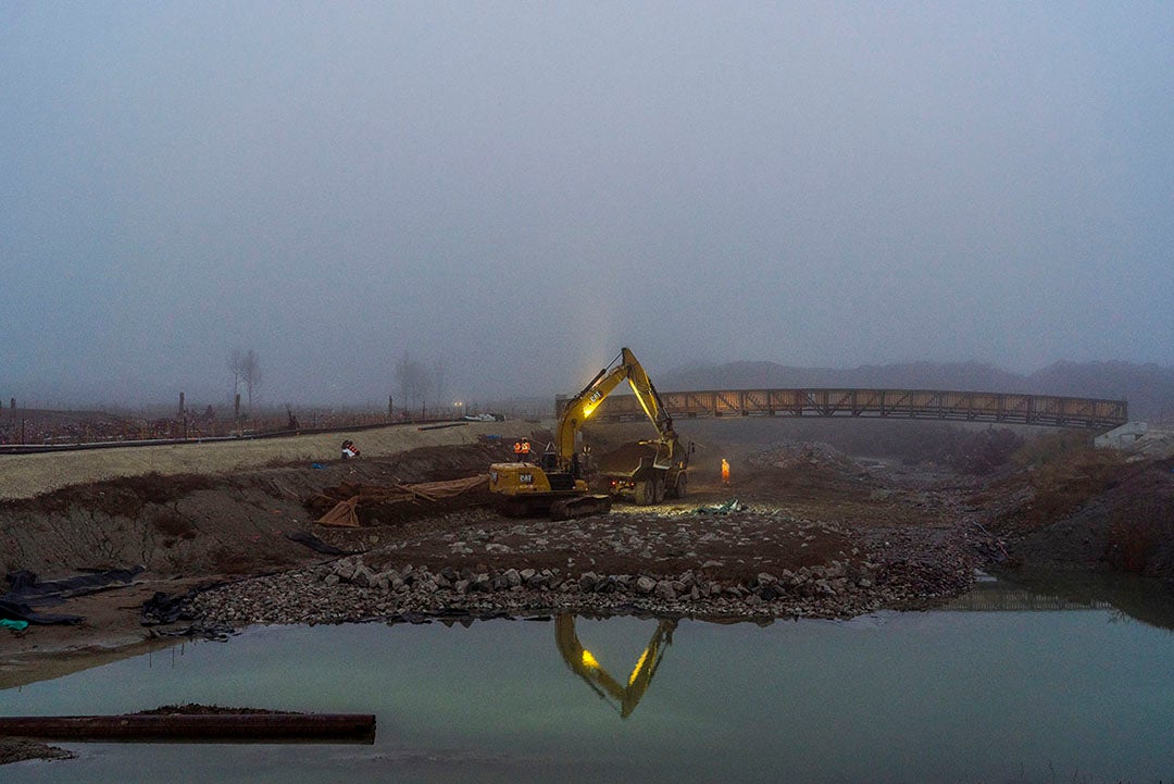 An excavator removes dirt to create a new river valley during the early morning.