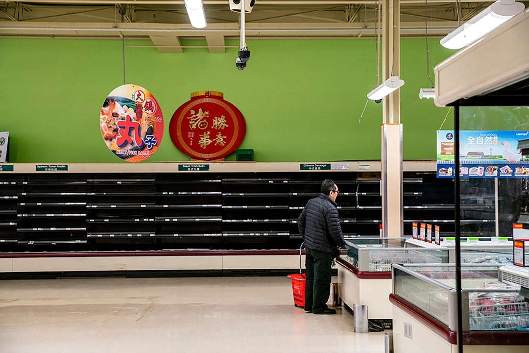 A person shops in a grocery store with empty shelves. 