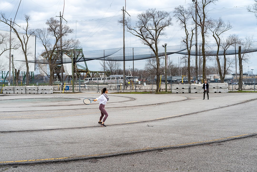 Two people play tennis in a paved court.