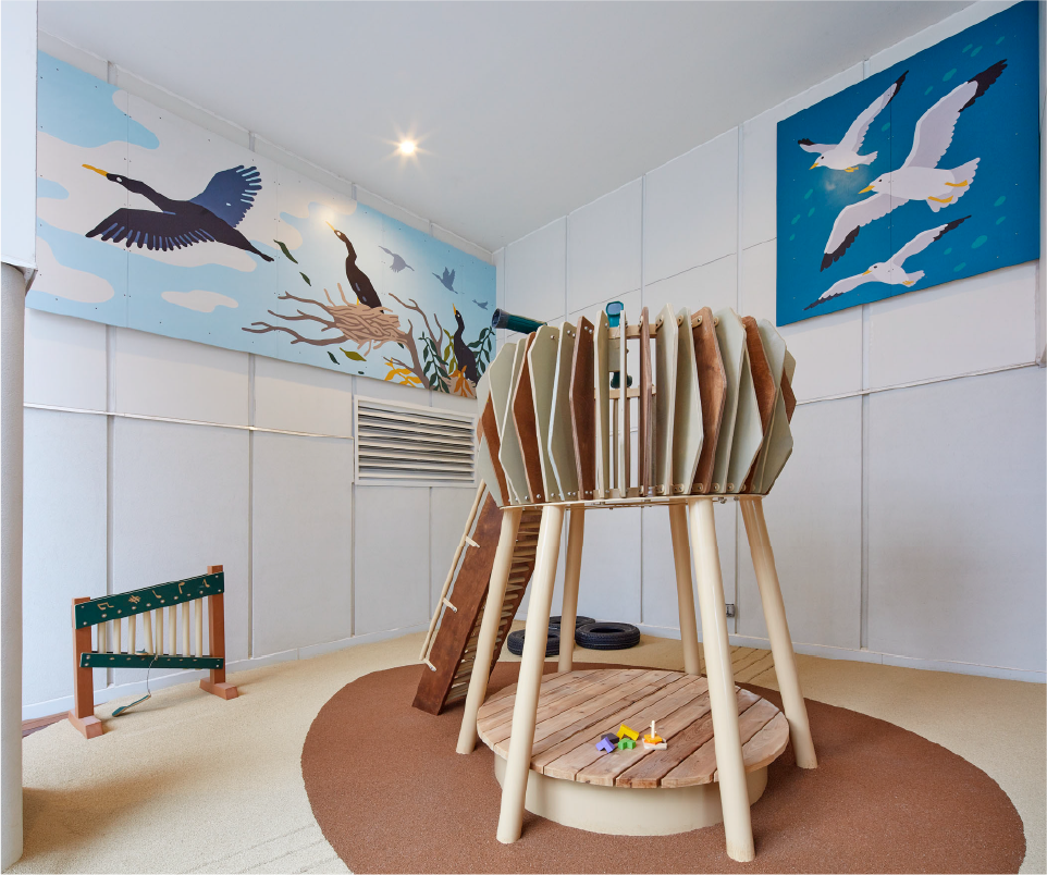 A wooden climbing structure with bird murals in the background. 