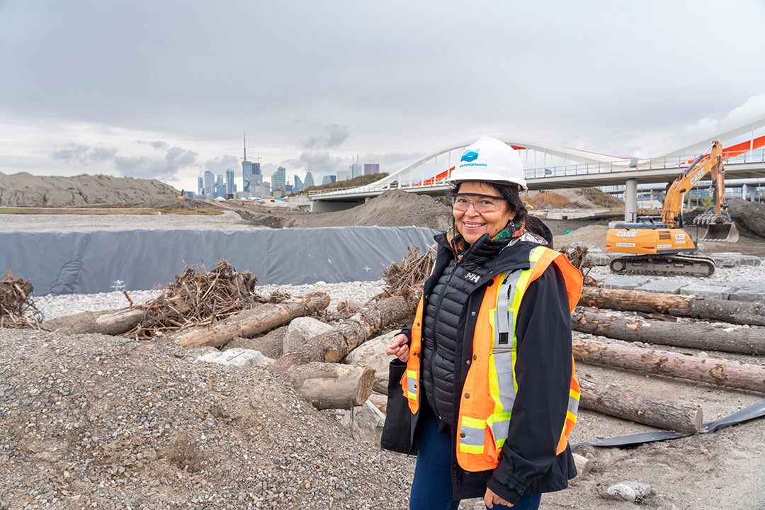 A person in construction protective gear smiles at the camera on a construction site.