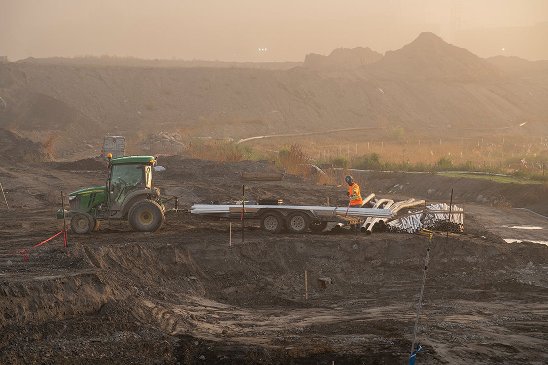 A tractor pulls pipes in a construction site.