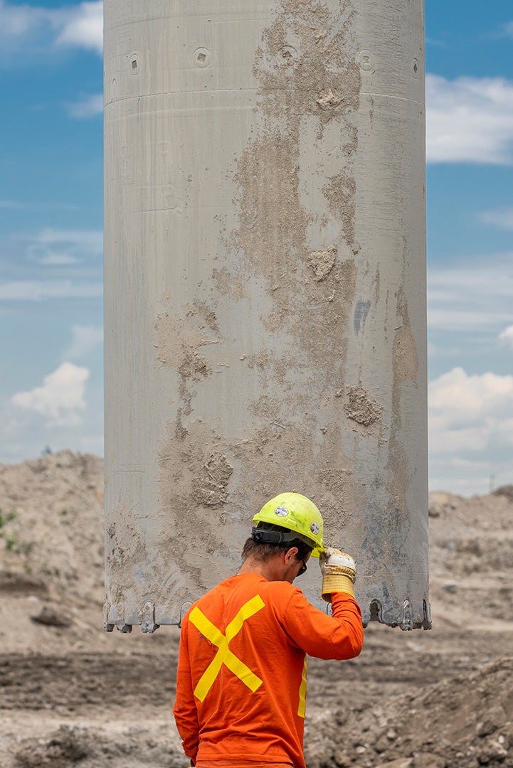 A construction worker stands in front of a cement cylinder.
