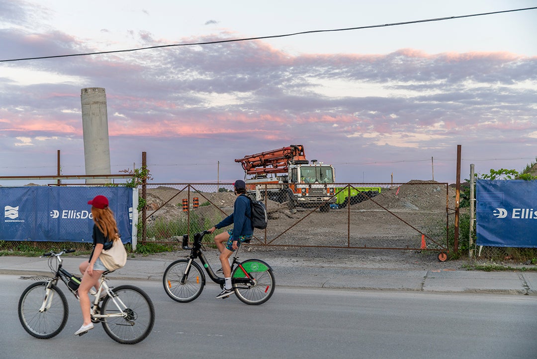 Two bikers bike by a construction site during sunset.