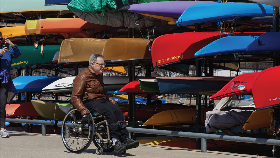 A person in a wheelchair with canoes on storage racks in background.