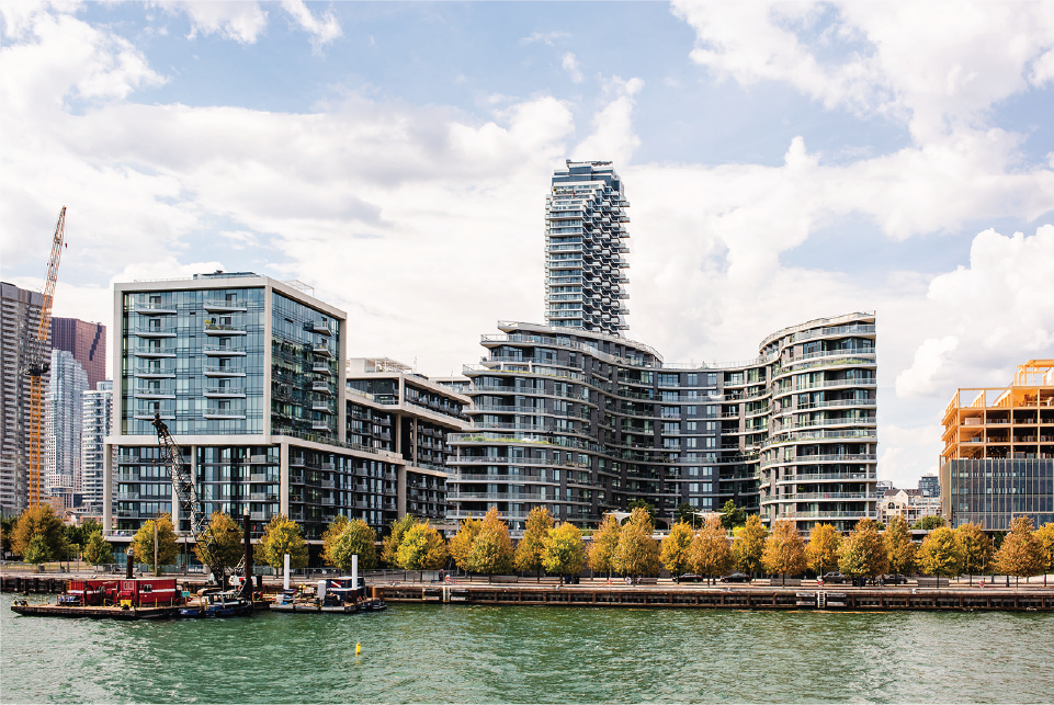 A tree-lined promenade with condo building in background and lake in foreground.