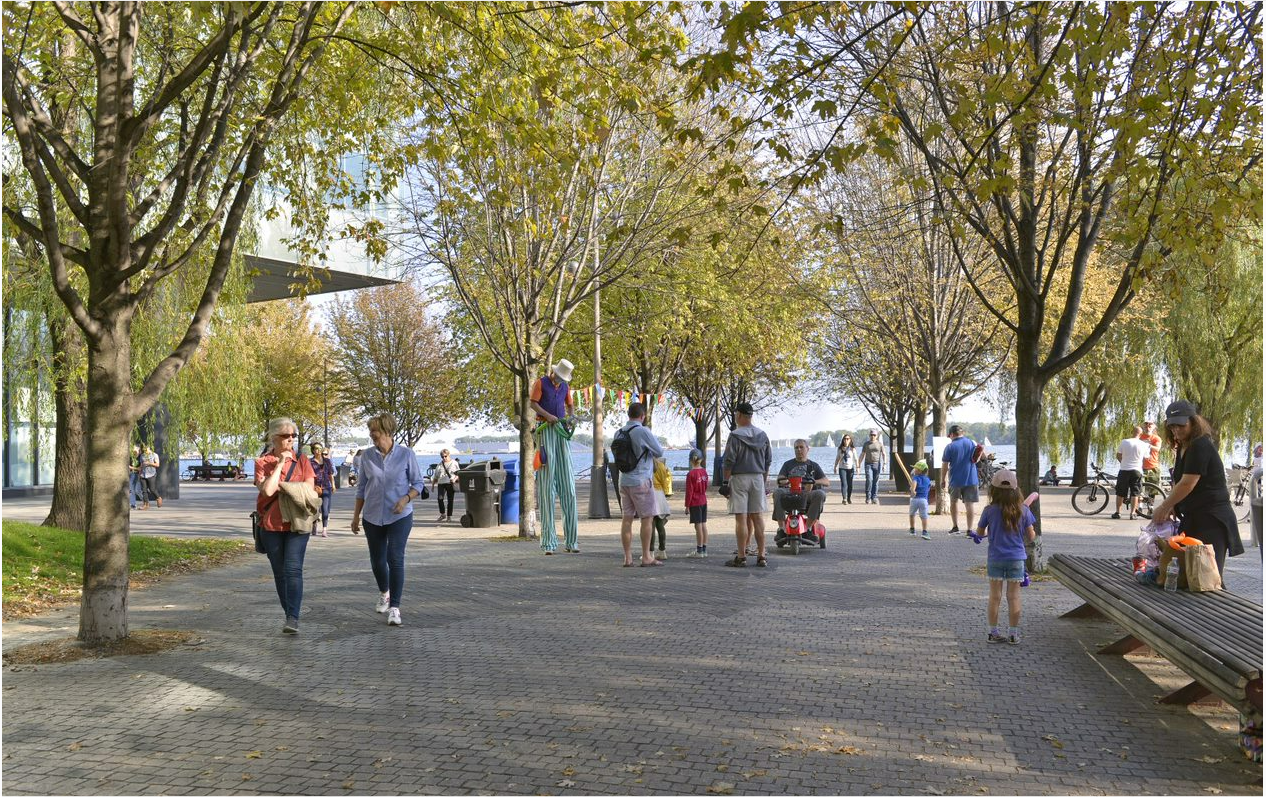 People traveling along a public promenade, with a lake in the background. 