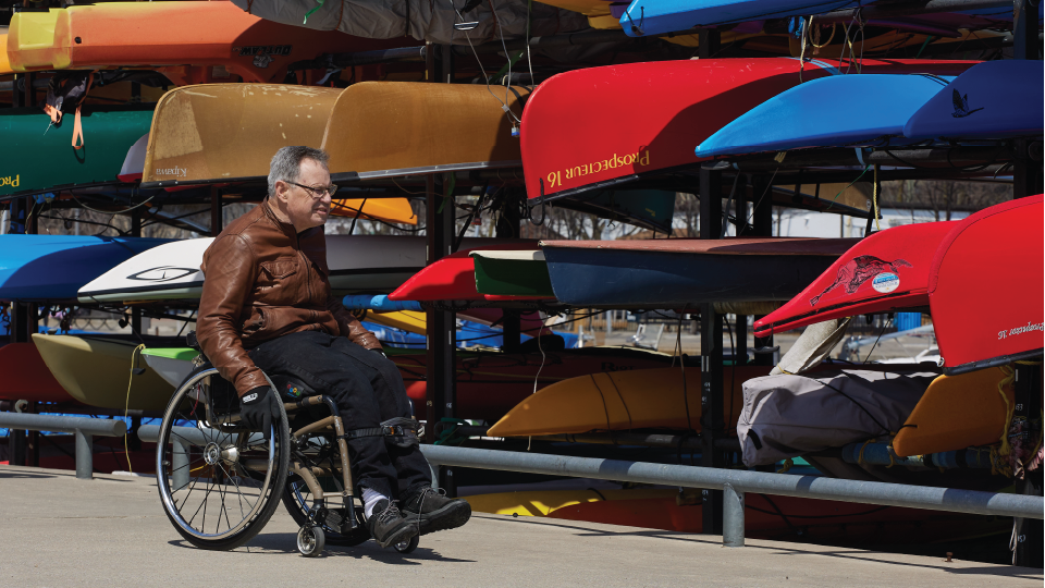 A person in a wheelchair, with canoes and kayaks in the background.