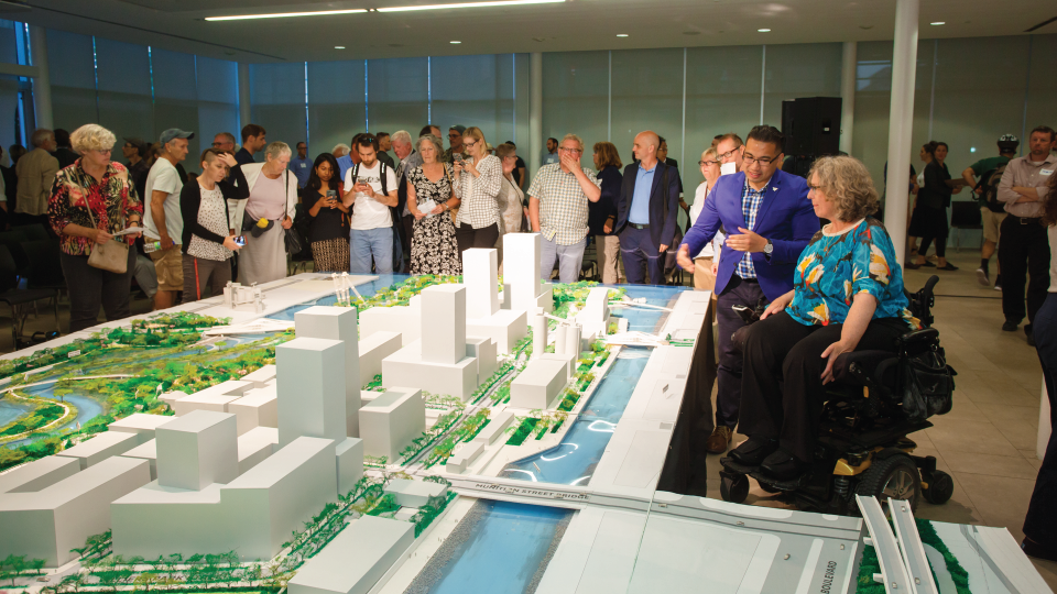People gathered around a model Villiers Island. One person is in an electric mobility chair.