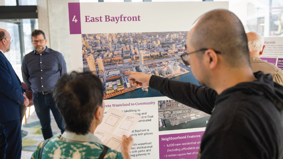 Two people in front of an informational poster, titled East Bayfront. 