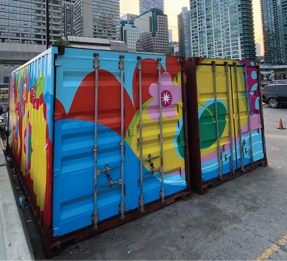 Two shipping containers covered in a vibrant mural. Downtown skyline in background. 