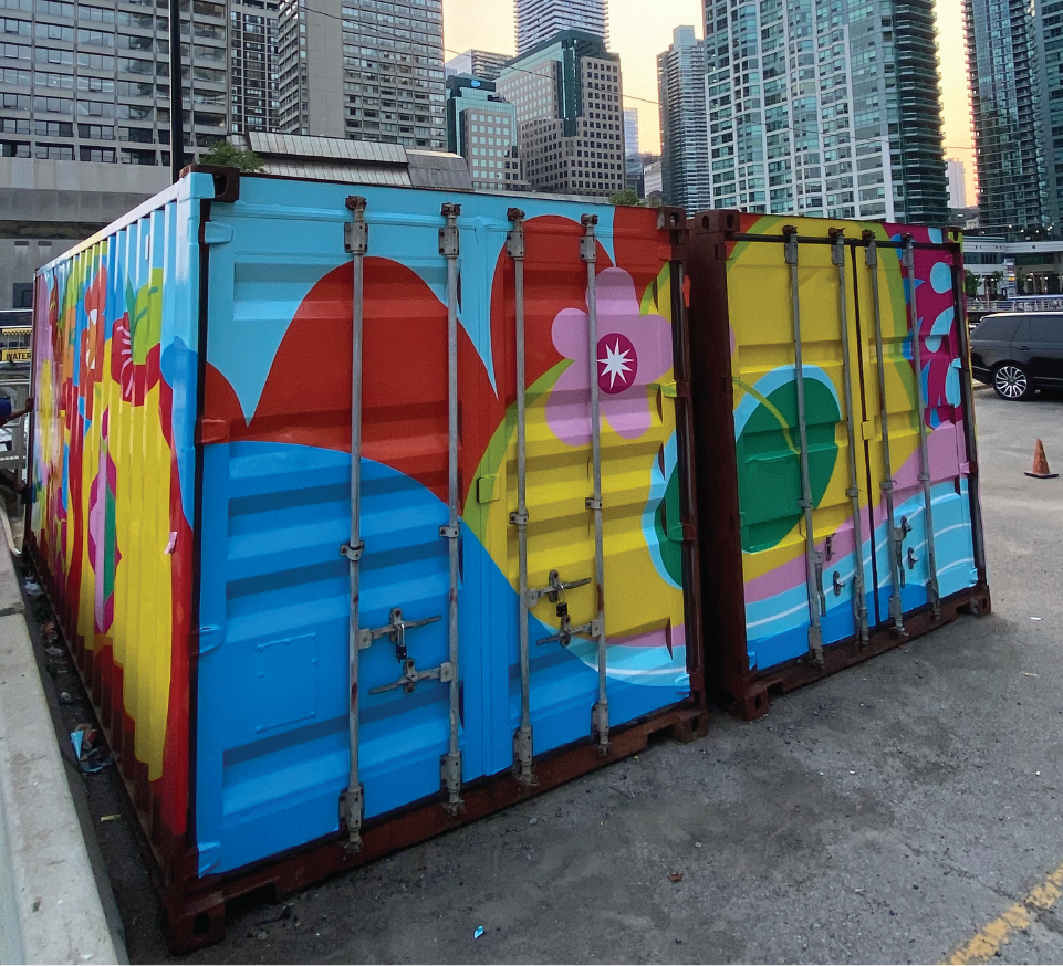 Two shipping containers covered in a vibrant mural. Downtown skyline in background.