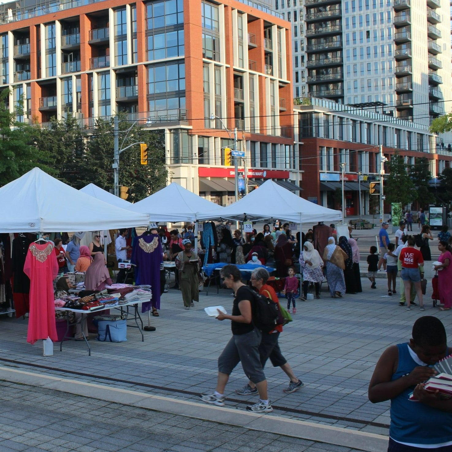 People attending an outdoor market with apartment buildings in the background. 