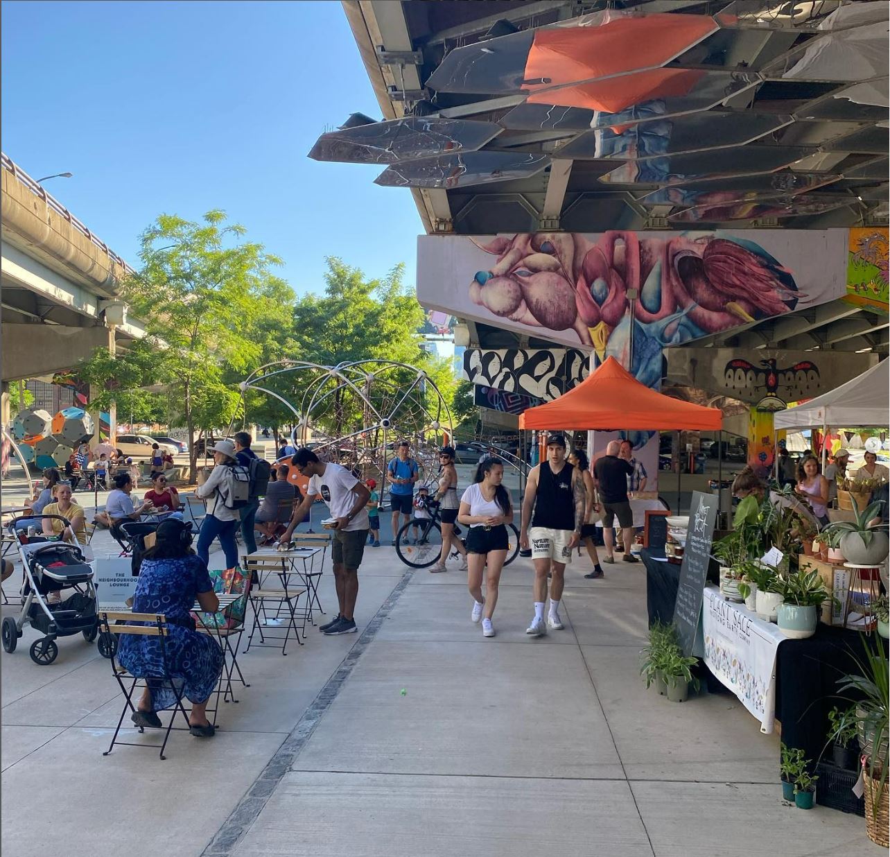 An outdoor farmers market under an elevated expressway. 