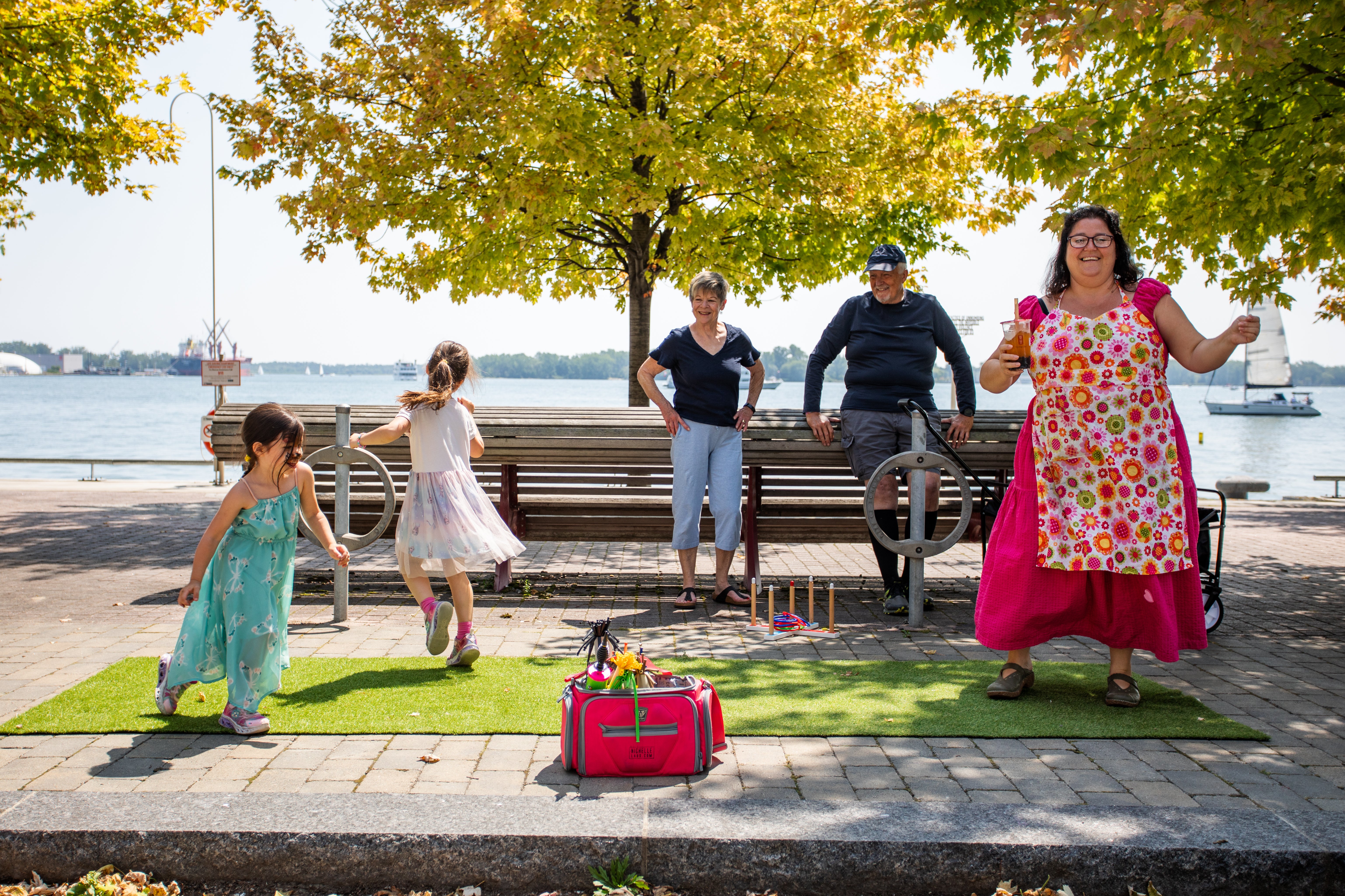 A woman and children dance in a public space on a sunny day by the water.