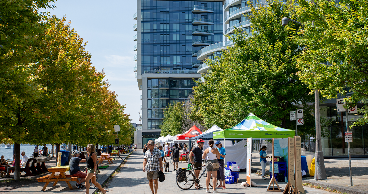 People enjoy a market along a promenade on the waterfront.