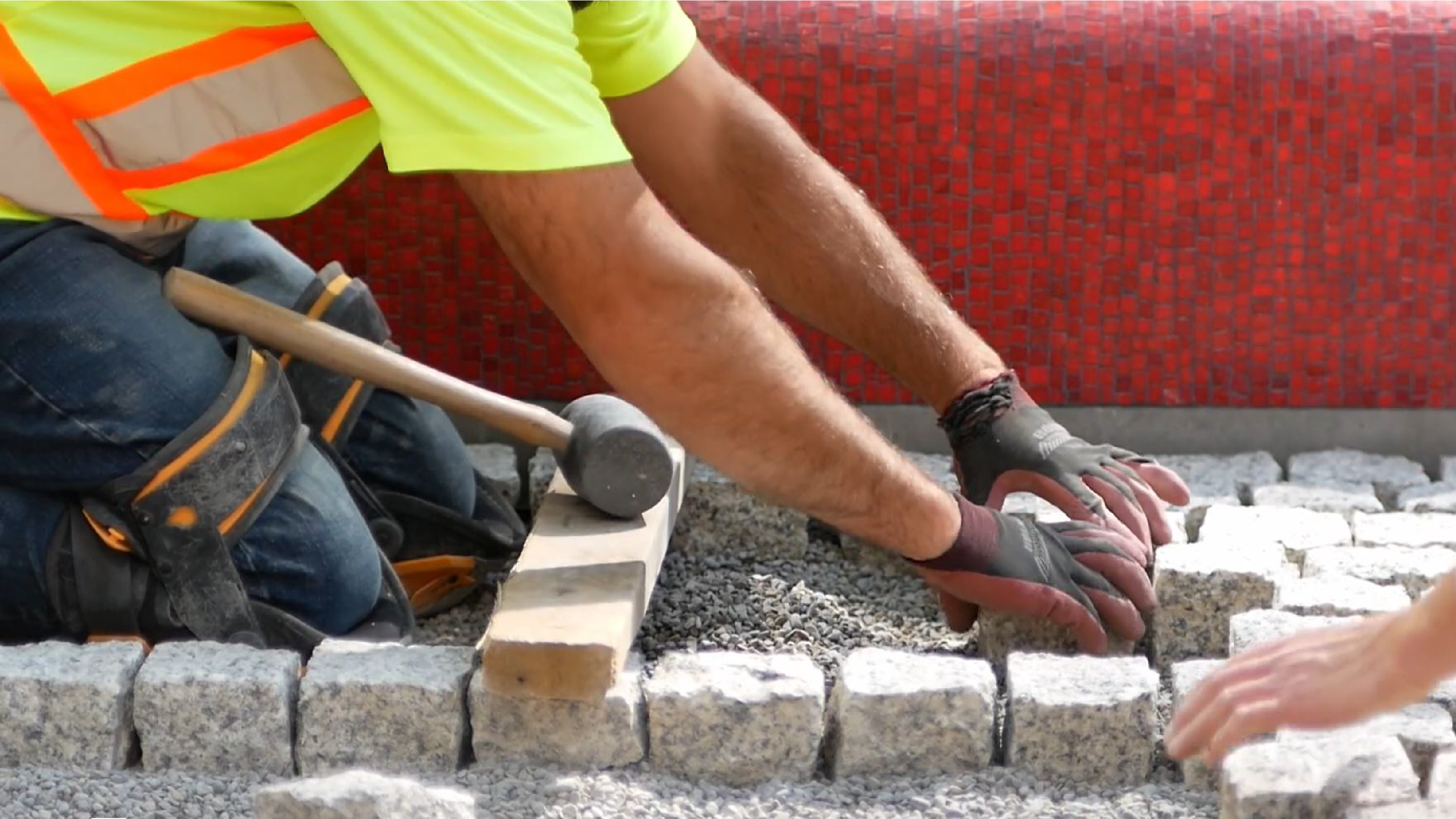 A mason laying granite pavers in a park under construction.