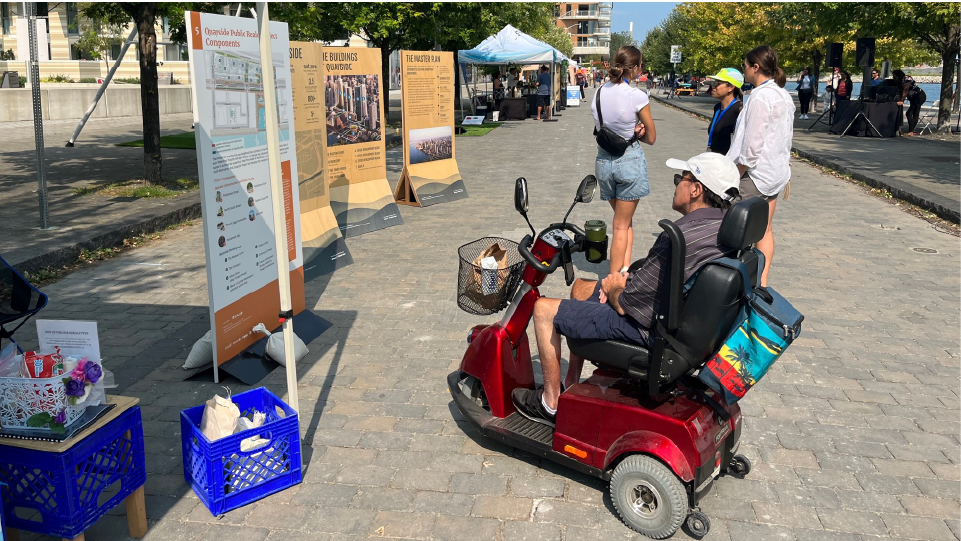 A person using a scooter reads a display board at a pop-up booth.