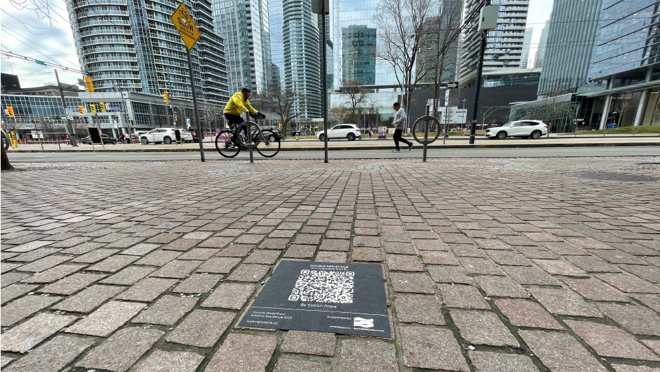 A Q R code decal on a Queens Quay sidewalk.