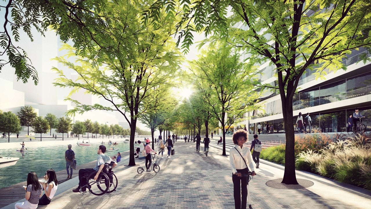 A bustling city promenade beside the water with pedestrians walking and cyclists biking through the urban landscape.