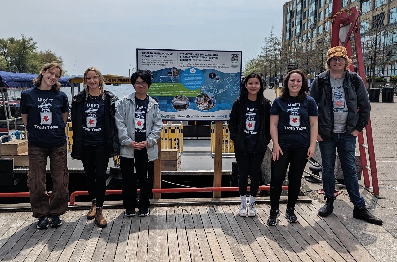 Group of six individuals wearing "U of T Trash Team" T-shirts standing in front of a board about water ecosystems.