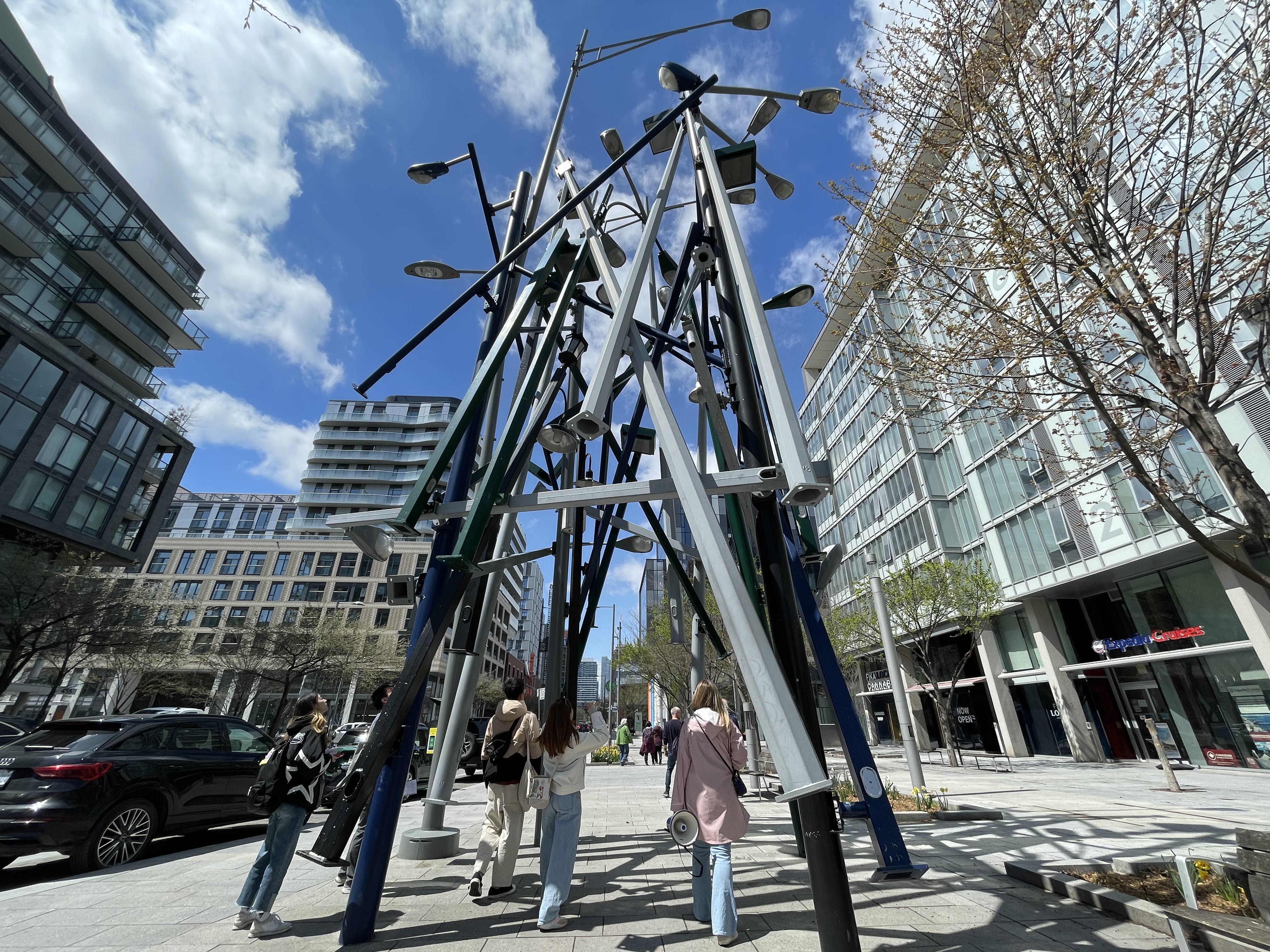 People observing Untitled (Toronto Lamp Posts) in West Don Lands on a bright sunny day.