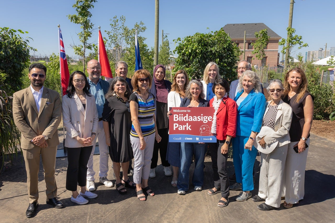 Group photo from the official opening of a new waterfront park in the Port Lands. One dignitary holds a sign saying "Welcome to Biidaasige Park".
