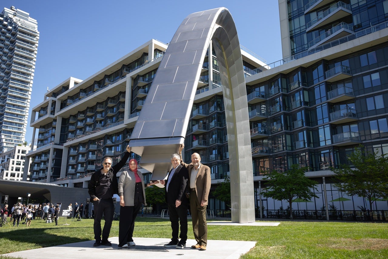 Four people pose next to a large arch - public art installation at the official unveiling in Sherbourne Common.