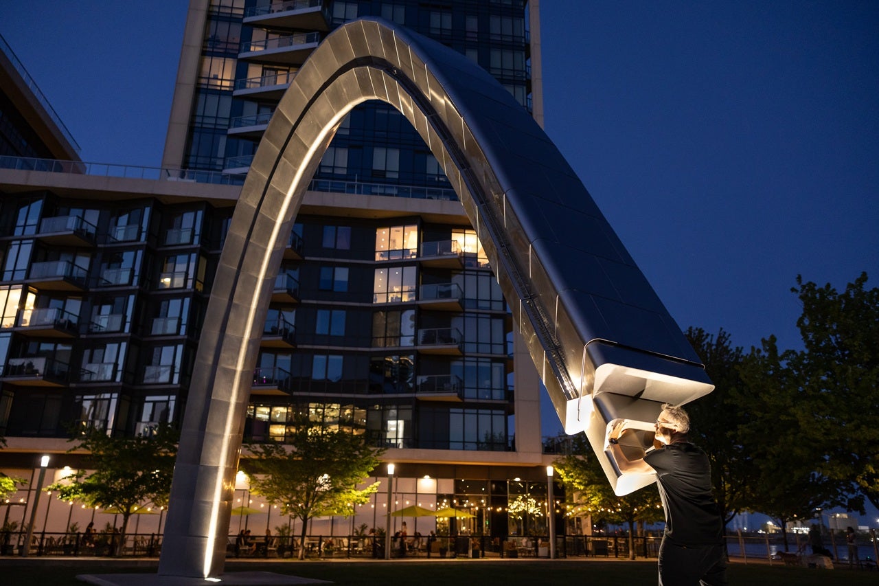 An artist activates a large public arch installation called - Unfinished Arch at night.