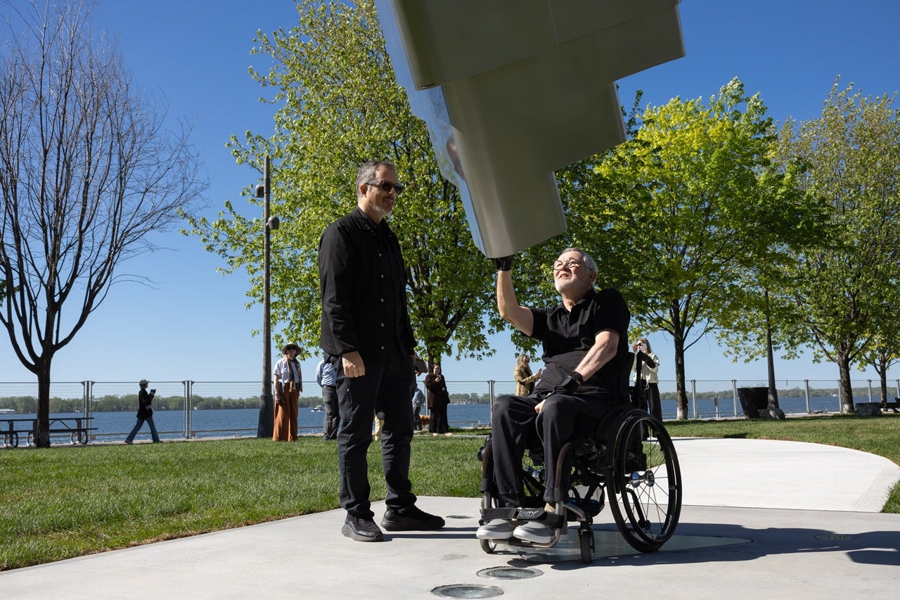 A person who uses a wheelchair tests out a new public art "arch" feature. Standing next to him is the artist.