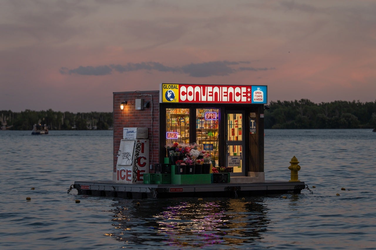 Floating artwork at night which appears to be a convenience store in the lake.