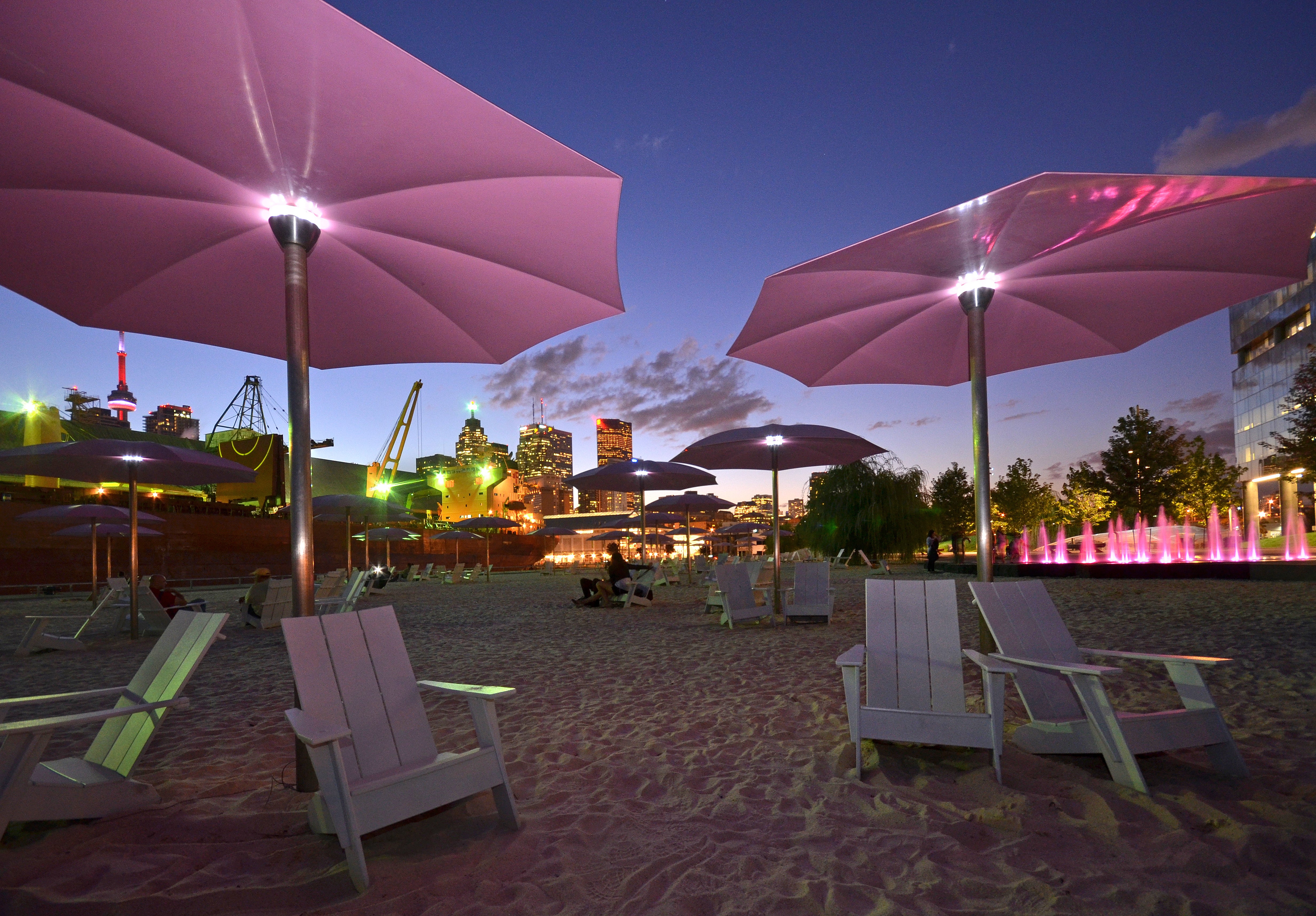 sandy urban waterfront beach with pink umbrellas at dusk