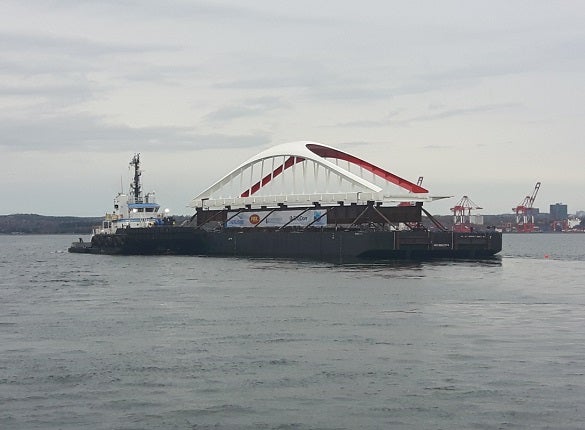 a white and red bridge being transported in the water on a barge